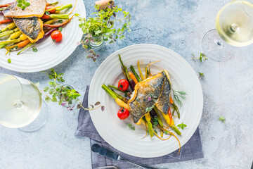 top view of delicious fish with vegetables on white plates and wine glasses on grey surface