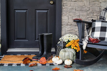 Traditional Style Front Porch Decorated For Autumn With Rain Boots, Heirloom Gourds,  White Pumpkins, Mums And Rocking Chair With Buffalo Plaid Pillow And Throw Blanket Giving An Inviting Atmosphere.