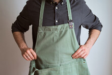 A Man In A Kitchen Apron. Chef Work In The Cuisine. Cook In Uniform, Protection Apparel. Job In Food Service. Professional Culinary. Green Fabric Apron, Casual Stylish Clothing. Handsome Baker Posing