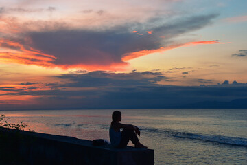 Wall Mural - Silhouette of girl sitting by the sea at sunset