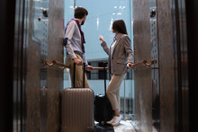 Businesswoman Showing Something To Her Male Colleague Outside Of A Glass Elevator