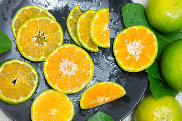 The tangerine sliced is placed in a black plate and the rim of the dish has orange and green citrus leaves along with a sprinkling of water for a refreshing look.