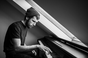 Musician and composer in a hat plays piano, black and white, The pianist performs a musical work on the piano, man  bw photo