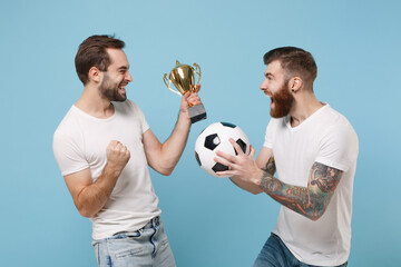 Happy two men guys friends in white t-shirt isolated on pastel blue background. Sport leisure lifestyle concept. Cheer up support favorite team with soccer ball, football cup doing winner gesture.