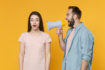 Wall Mural - Crazy young couple two friends guy girl in pastel blue casual clothes posing isolated on yellow wall background. People lifestyle concept. Mock up copy space. Scream in megaphone, keeping eyes closed.