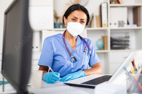 Female doctor in face mask listening to patient complaints at clinic
