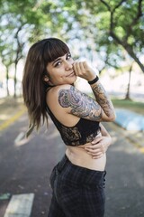 Poster - Young attractive Caucasian female with tattoos standing in the park and making a cute face