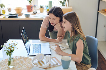 Mother watching how daughter working with other students in group video chat with teacher