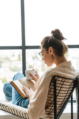 Wall Mural - Image of thinking cute woman reading book and drinking coffee