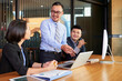 © DragonImages - Professional business analyst demonstrating stats to colleagues on laptop in modern office board room during meeting