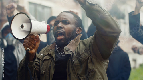 Fotografía African-American young handsome man screaming in megaphone at protest for human rights outdoors in smoke