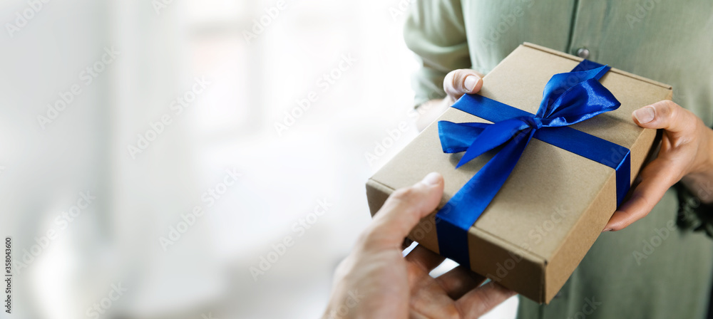hand giving gift box with blue ribbon to a woman. copy space - obrazy, fototapety, plakaty 