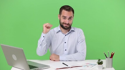 Young bearded business man sit work at desk with pc laptop computer isolated on green background studio Achievement business career lifestyle concept rubbing fingers showing cash gesture asking money