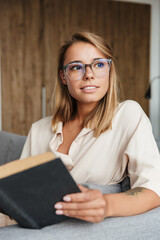 Poster - Image of young pleased woman reading book while sitting on couch