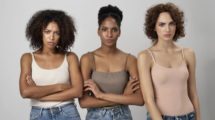 Wall Mural - three serious multi-ethnic women are showing silence gesture standing isolated over white background