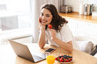 Photo of woman using laptop and eating strawberry while having breakfast