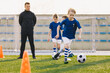 © matimix - Sports physical education lesson. Children training soccer football on schools field. School athletic activities. Sports education for kids and youth. Young coach coaching junior level team