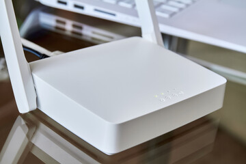 White wireless wi-fi router near a laptop on a glass table