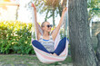 © Kyryl Gorlov - Young adult happy short haired shaved bald attractive woman chilling enjoy relaxing sitting in fabric chair hammock at yard in garen near house. Peaceful and idyllic outdoor rest lifestyle