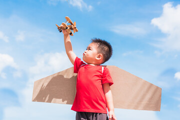 Wall Mural - Happy Asian funny child or kid little boy smile wear pilot hat play and goggles with toy cardboard airplane wing flying hold plane toy outdoor against summer blue sky cloud background, Startup freedom