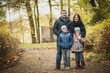 © Chendekova Liudmila - A cute family is standing in the autumn park with orange foliage. The wife lies on her husbands chest, Daughter hugs her mother, the son is standing next to him. Beautiful portrait, soft focus.