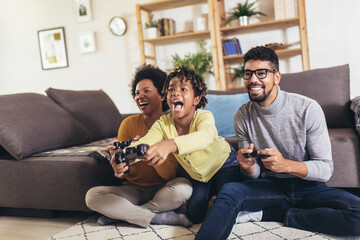 African American family at home sitting in sofa couch and playing console video games together