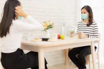 Wall Mural - Young Asian  woman sitting separated in restaurant or home  eating food with table protect infection from coronavirus covid-19, new normal restaurant and social distancing concept.