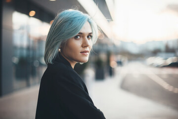 Charming caucasian woman with blue hair looking back at camera while cheering outside in the street