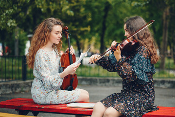 Girls in a summer park. Two ladies with a violin. Friends sitting on a bench