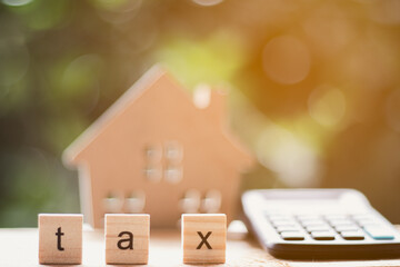 Wooden blocks with the word TAX with blurred calculator, wooden house toys with blurred green background - tax concept.