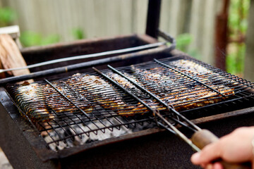 Wall Mural - Men grilling fish mackerel on barbecue cooked on the grill in the open air flow, tasty and fresh food, picnic, party, outdoor recreation. Barbeque in the garden in summer at home. .