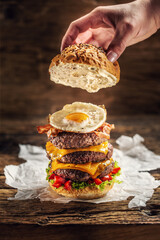 Canvas Print - Hand putting the top of bun on a triple cheeseburger with beef patty, egg and peppers in a rustic wooden environment