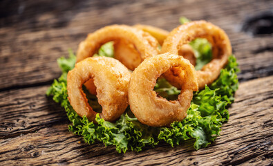 Canvas Print - Cripsy onion rings on a lettuce leaf placed on a rustic wood