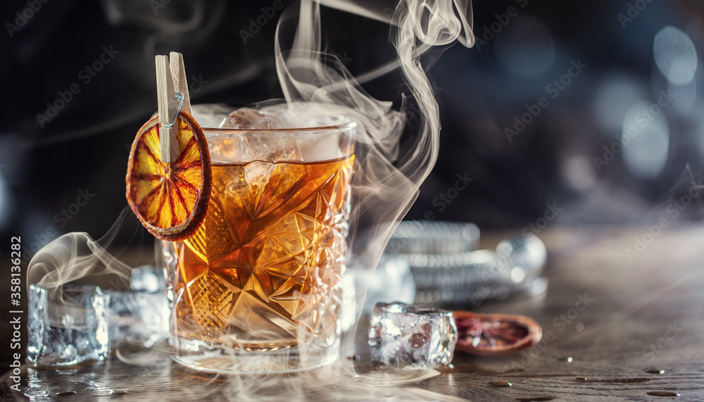 Smoked old fashioned rum cocktail with cubes of ice around on a dark background - obrazy, fototapety, plakaty 