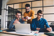 © BullRun - Millennial hipster guys collaboration together in coworking space sitting at desktop with laptop while one of them making photos of computer screen, man reading sms message via digital tablet