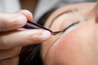 © Михаил Решетников - Woman lies on eyelash extension procedure in a beauty salon. Lashmaker holds tweezers with a bunch of artificial eyelashes. Close-up of a craftsman in gloves.