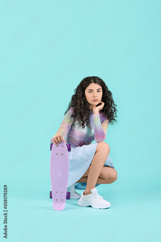Beautiful young woman with skateboard on color background