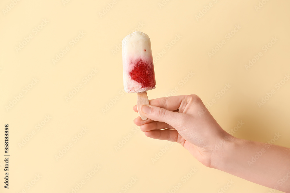 Hand with tasty strawberry ice cream on color background