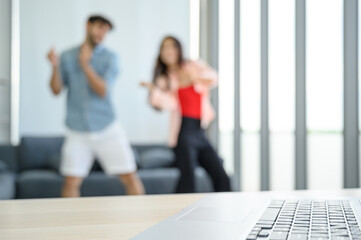 Laptop notebook computer on the table with happy and relax young couple lover wearing casual dress together dancing in living room at home.