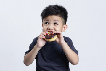 Little happy cute boy is eating donut on gray background. child is having fun with donut. Tasty food for kids