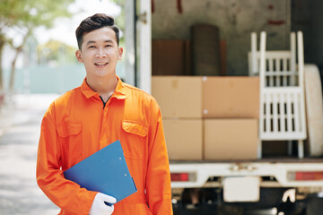 Sticker - Horizontal medium portrait of young adult Asian moving man wearing bright orange uniform standing outdoors holding blue clipboard, copy space