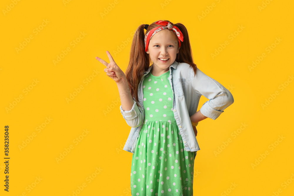 Cute redhead girl showing victory gesture on color background