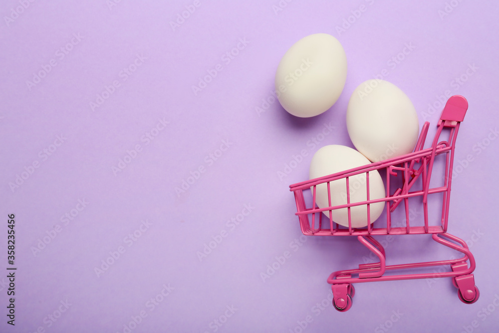 Shopping cart with chicken eggs on color background