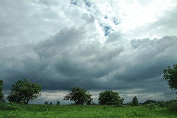 Wall Mural - thunderous epic clouds in a field near the old garden. stock photo background with heaven.