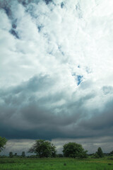 Wall Mural - thunderous epic clouds in a field near the old garden. stock photo background with heaven.