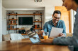 © bnenin - Smiling man reading a letter at home, sitting at the table and his wife using laptop.