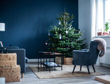 Christmas Tree In The Interior. Scandinavian Style, Minimalism. Dark Blue Wall, Grey Chair, Braided Baskets. White Paper Origami Toys.