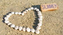 Heart-shaped Snail Shells On The Sand. The Words "summer" On A Wooden Crossbar. Space For Text. Love Story And Background. Romantic Vacation On The Beach. Symbol Of Love. Concept For The Summer Period