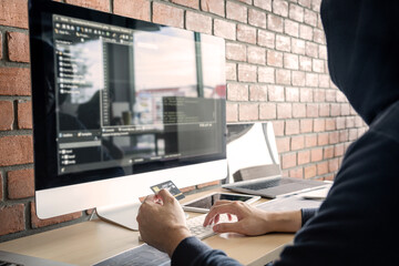 Wall Mural - computer hacker or cyber attack concept, dangerous hooded hacker using multiple computers typing bad