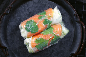 Top view of two pieces of traditional Vietnamese spring rolls filled with salmon, avocado, salad and rice noodles on dark plate